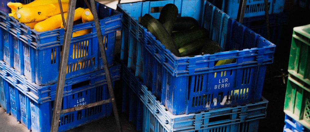 Blå plastbackar med gul squash och zucchini vid ett marknadsstånd